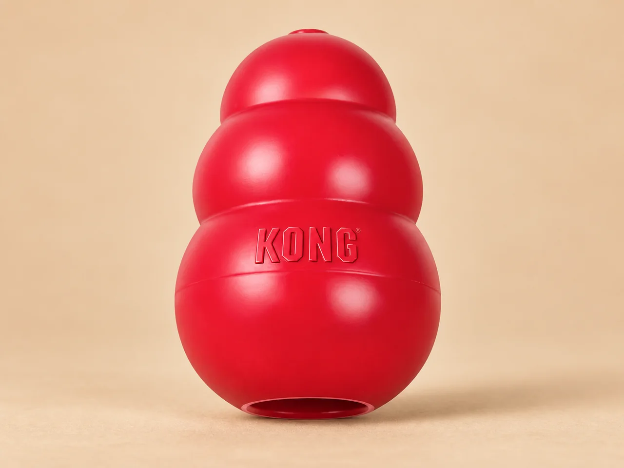 웜 베이지 배경 위에 서 있는 빨간 KONG Classic 천연 고무 장난감