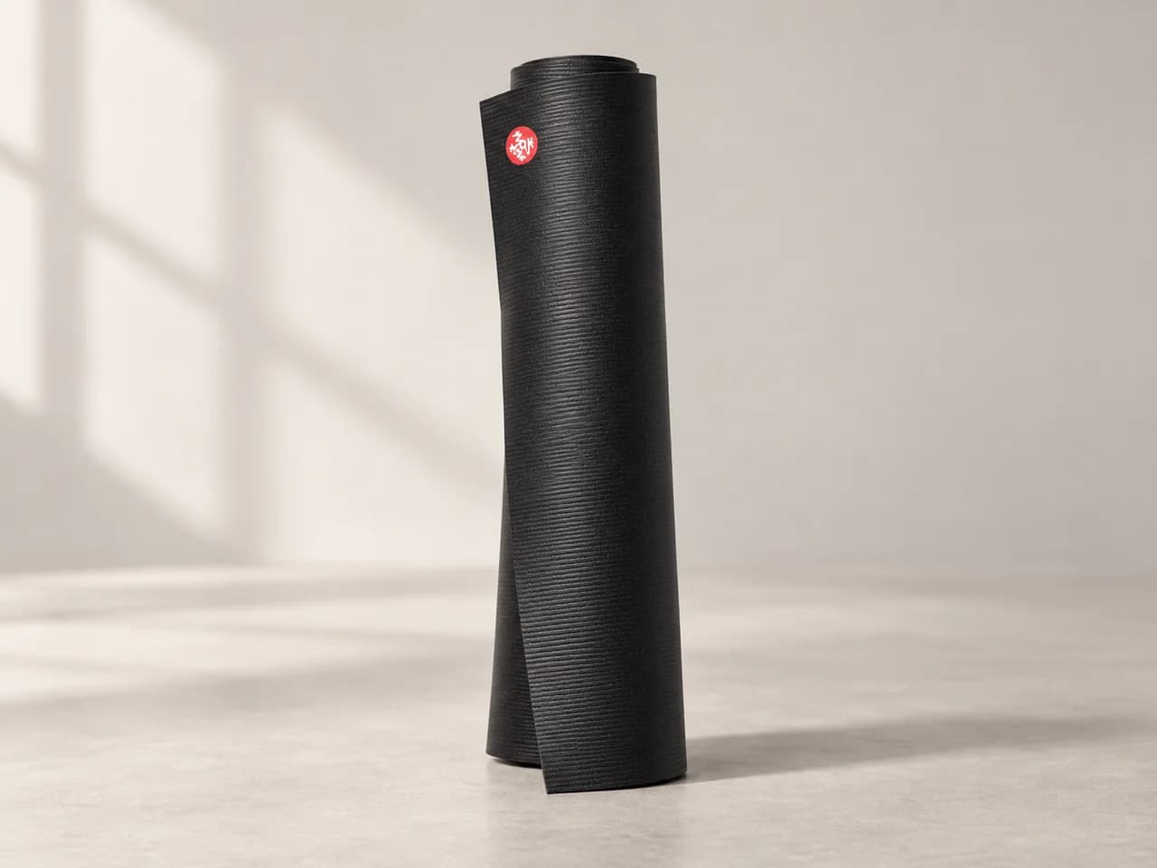 창가 빛이 드는 스튜디오 바닥에 세워 둔 블랙 Manduka PRO 6mm 요가 매트